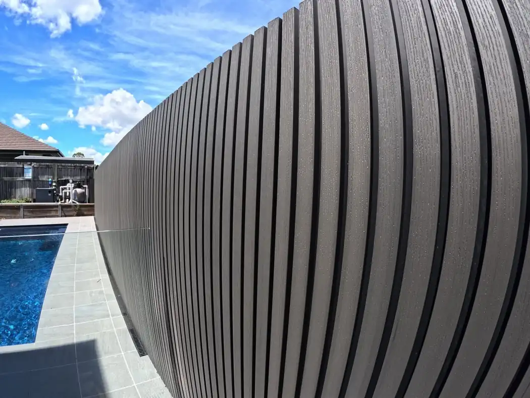 Dark composite batten screen curving around a swimming pool surround